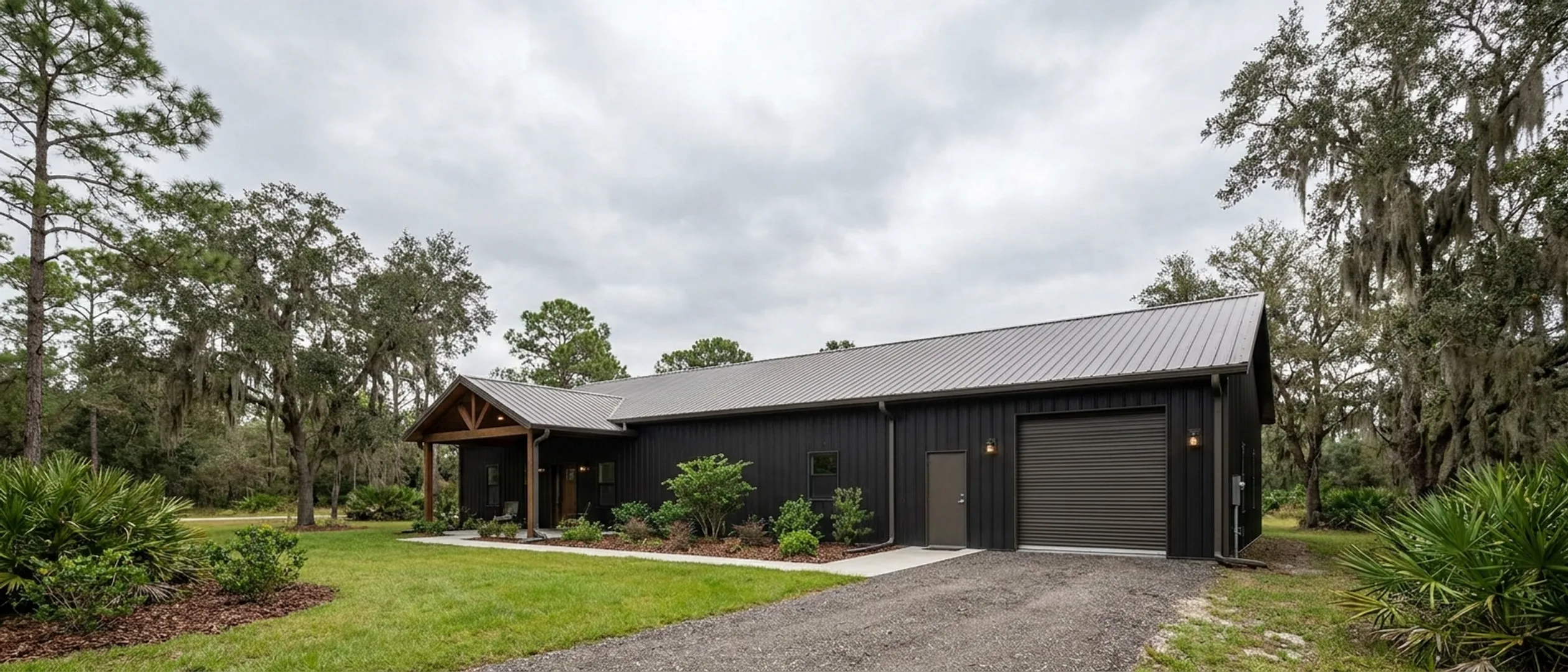 A completed barndominium with a covered entry porch and an attached shop bay, photographed in flat overcast daylight.