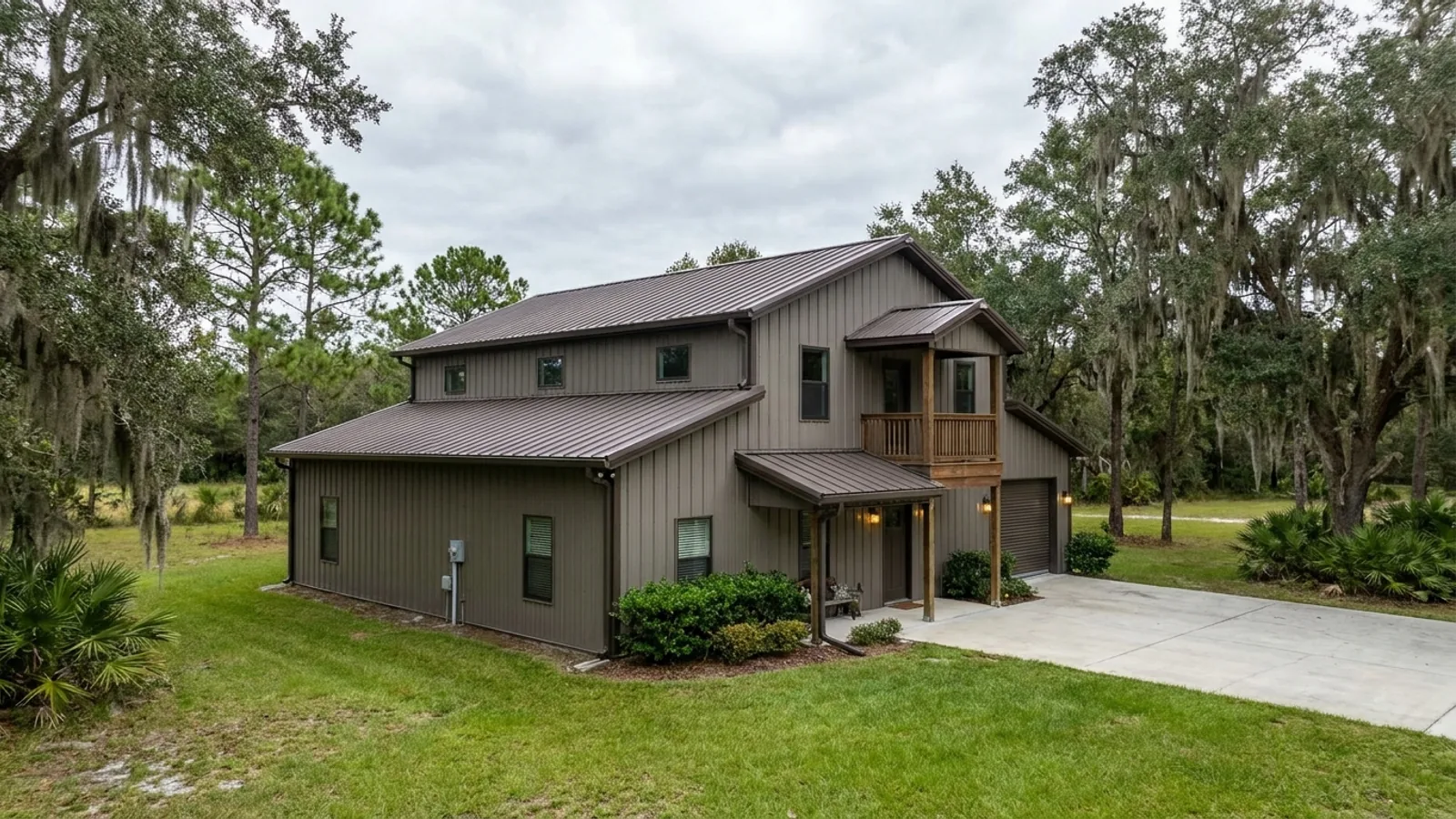 A completed two-story barndominium with visible second-story windows and a small covered balcony above the entry porch.